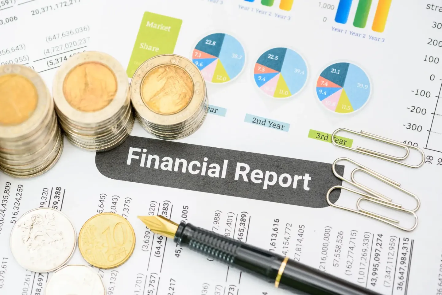 Coins stacked on a financial report with charts and a pen.
