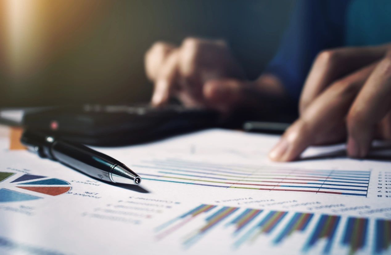 Person analyzing financial charts with pen and calculator.