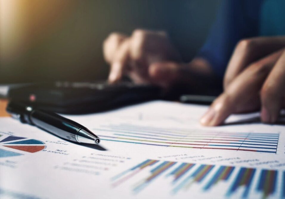 Person analyzing financial charts with pen and calculator.