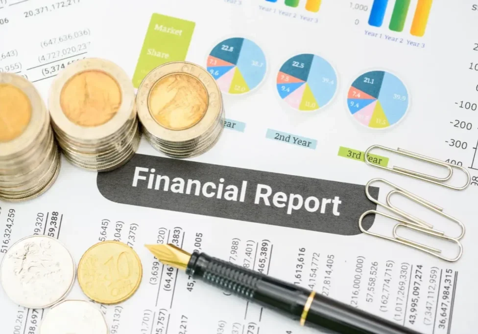 Coins stacked on a financial report with charts and a pen.